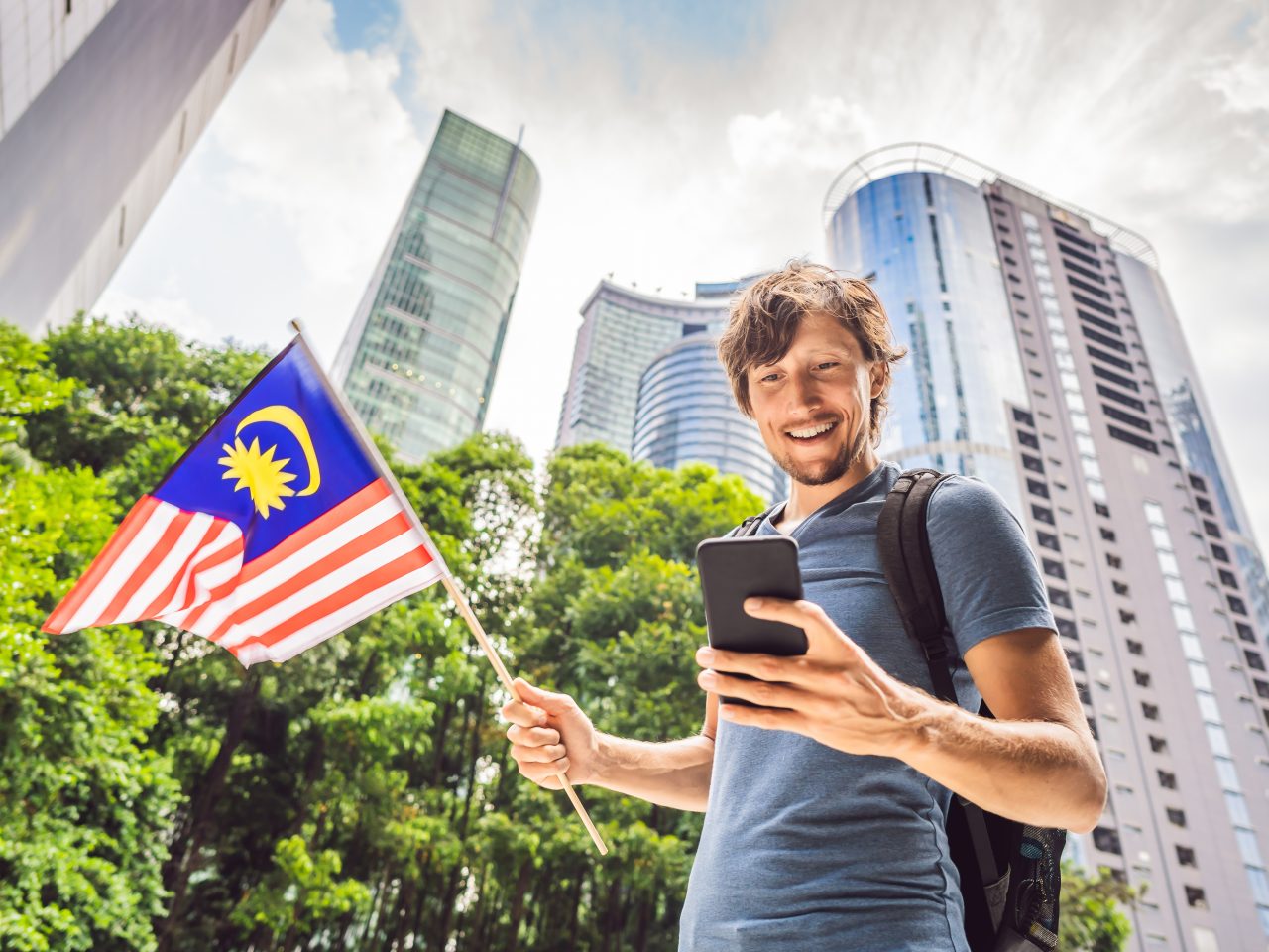 Travel and technology. Young man tourist with the flag of Malaysia is looking at a city map in a smartphone for navigation.